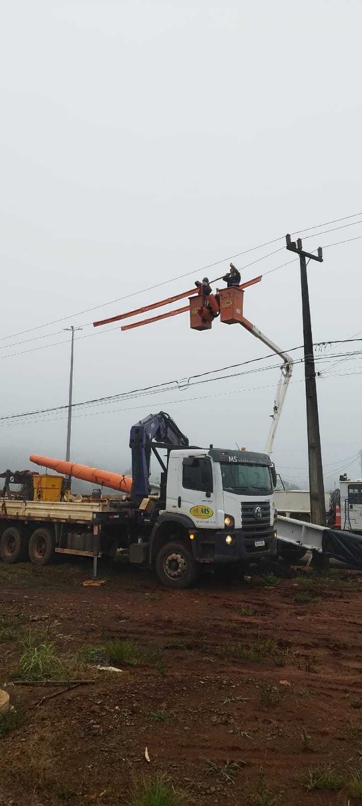 Equipe linha viva da MS Engenharia Elétrica em cestos aéreos laranjas trabalhando na rede de média tensão, com caminhão munck da empresa