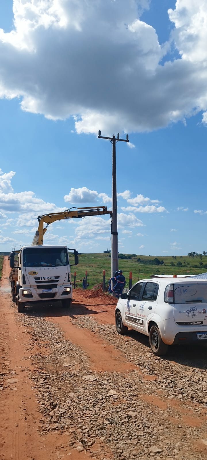 Caminhão munck da MS erguendo poste em estrada rural